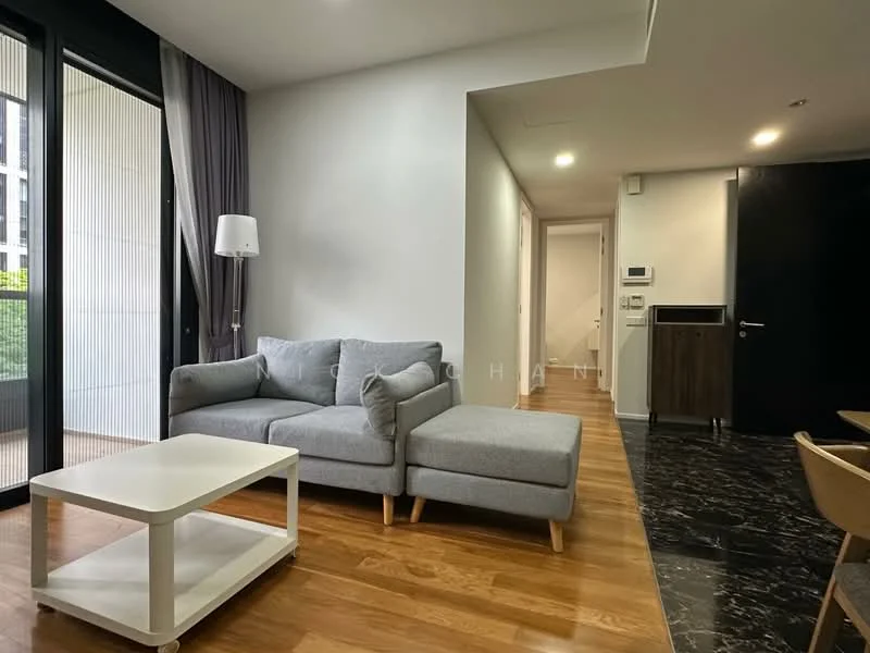 Living features: grey fabric sectional sofa, white coffee table, wooden flooring, floor-to-ceiling windows, curtains, wall-mounted light, decorative wall panel, open layout to hallway; style: modern; view: garden. Room features: white painted walls, wooden flooring, doorway leading to hallway, light switch panel.
