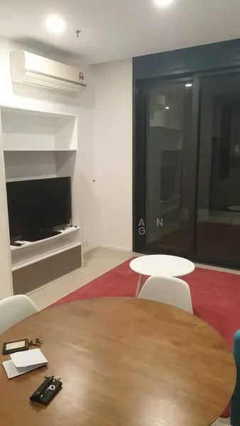 Living features: wall-mounted TV, white TV console, light wood dining table, white dining chairs, red area rug, air conditioning unit, large glass sliding door, neutral painted walls, tile flooring, small round coffee table; style: modern.
