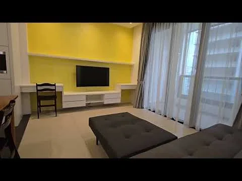 Living features: yellow painted walls, floor-to-ceiling windows with sheer curtains, light-colored tile flooring, flat-screen TV mounted on wall, white TV console, dark grey fabric sofa, coffee table with tufted design, wooden chair, decorative shelving unit, recessed lighting; style: modern.
