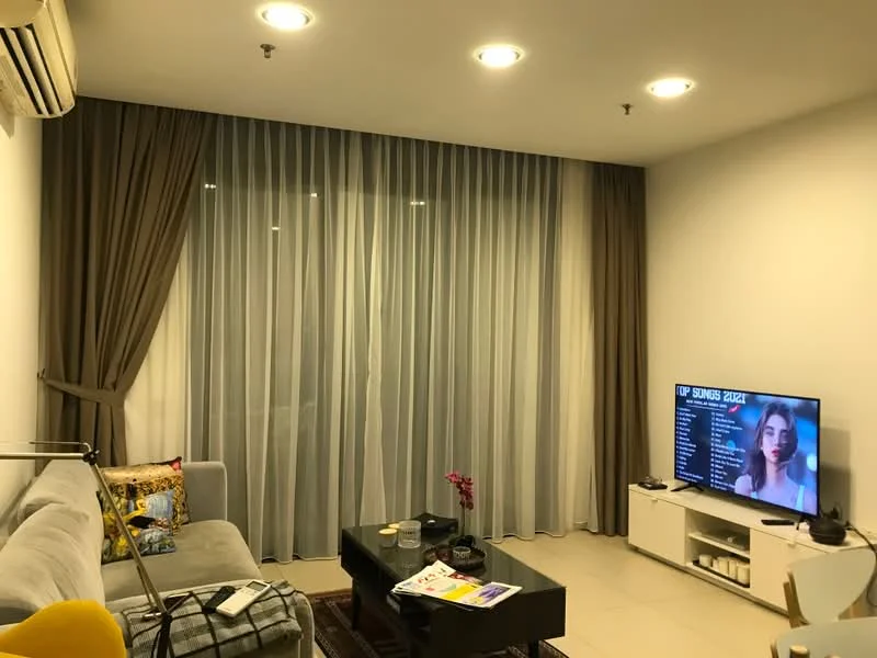Living features: grey fabric sofa, coffee table, wall-mounted TV, floor-to-ceiling windows, sheer curtains, dark brown curtain, recessed LED downlights, air conditioning unit, decorative throw pillows, magazines on coffee table, ceramic vase with flower; style: modern.