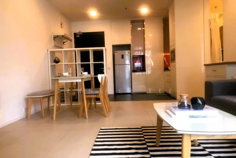 Living features: grey fabric sofa, coffee table with glass top, area rug with black and white stripes, dining table with four wooden chairs, wall-mounted TV, refrigerator, kitchen cabinetry with glossy finish, open layout, tile flooring, recessed lighting, neutral wall color, decorative items on coffee table; style: modern.