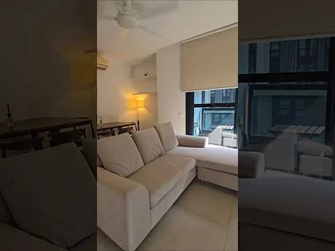 Living features: L-shape sectional sofa in light beige, floor-to-ceiling windows, roller blinds, ceiling fan, light source from lamp, neutral painted walls, tile flooring, small dining table, decorative items on table; style: modern; view: city.