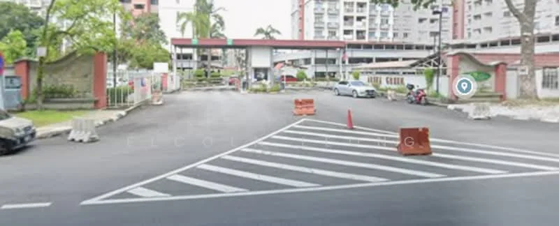 Exterior type: gated community entrance; features: guard house at entrance, boom gate, perimeter fence, paved driveway, traffic cones, landscaped greenery, surrounded by residential buildings, parking area visible; style: modern.