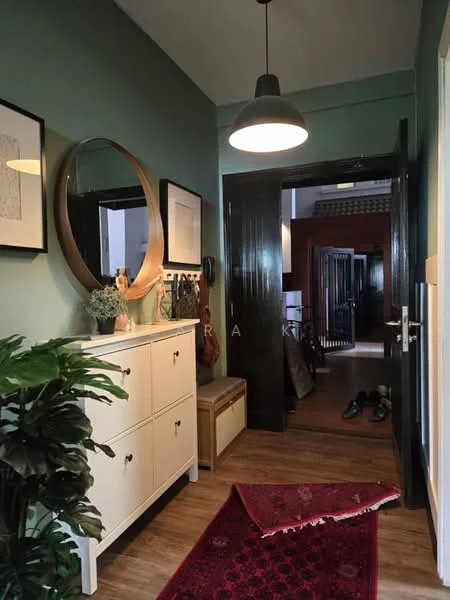 Room features: green painted walls, wooden flooring, pendant light, framed artwork, circular mirror, console table with drawers, decorative plant, area rug with geometric pattern, bench seating, door with black finish, shoe storage, wall hooks for accessories; style: modern.