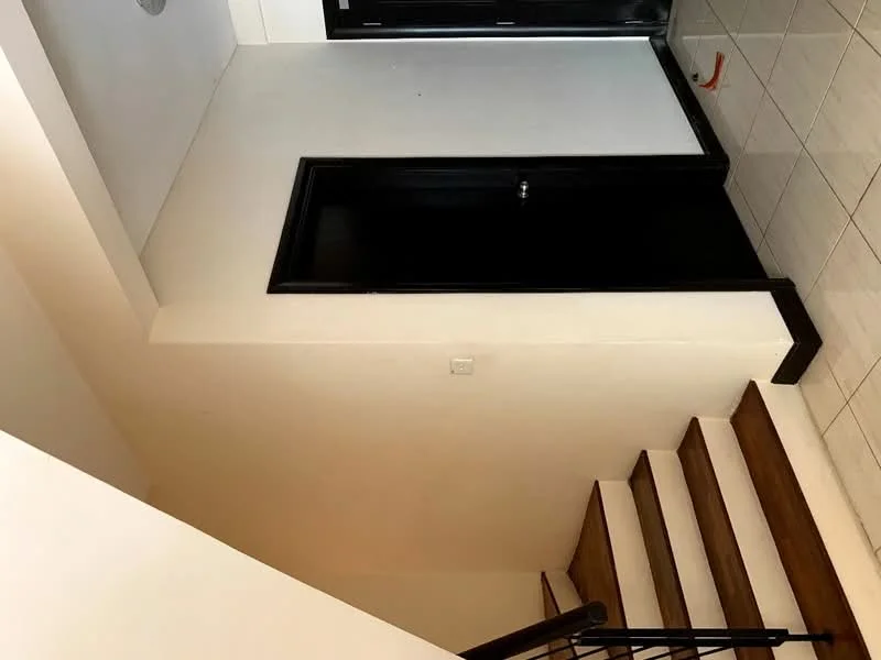 Room features: white painted walls, tile flooring, wooden staircase, black door, black railing, light fixture on ceiling; style: modern.