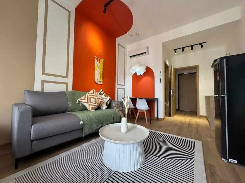 Living features: grey fabric sofa, green throw blanket on sofa, round coffee table with white base, black and white area rug with geometric pattern, red accent wall, cream painted walls, wooden flooring, wall-mounted air conditioning unit, recessed lighting, decorative wall art, white dining chair, black refrigerator, wooden door leading to hallway; style: modern.