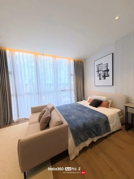 Bedroom features: king-size bed, upholstered headboard, bedside table, framed artwork on wall, floor-to-ceiling windows, sheer curtains, grey bedding, wooden flooring, area rug, decorative cushions; style: modern; view: city.