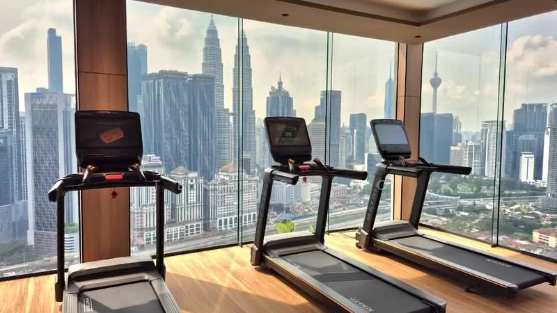Room features: treadmills, floor-to-ceiling windows, city skyline view, wooden flooring, modern fitness equipment, natural light, glass walls, urban landscape; style: modern; view: city.