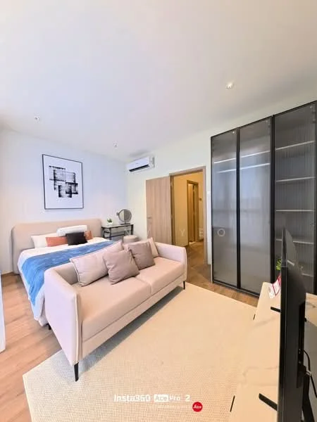Living features: light wood flooring, white painted walls, sofa in light beige fabric, area rug in cream, wall-mounted TV, built-in wardrobe with glass doors, air conditioning unit, framed artwork on wall, bed with blue and white bedding, decorative throw pillows; style: modern.