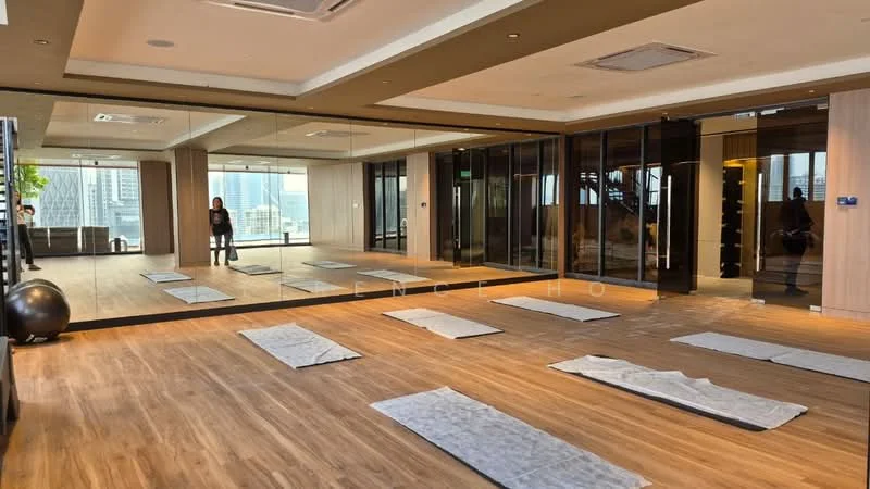 Room features: wooden flooring, mirrored wall, large windows with city view, recessed ceiling lights, air conditioning unit, exercise mats on the floor, open layout, greenery visible outside the window; style: modern; view: city.