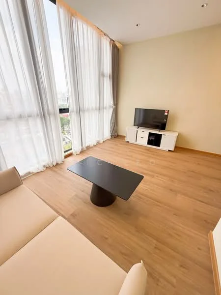 Living features: large floor-to-ceiling windows, sheer curtains, light grey walls, wooden flooring, 3-seater beige sofa, black coffee table, white TV console, wall-mounted TV, decorative items on console; style: modern; view: city.