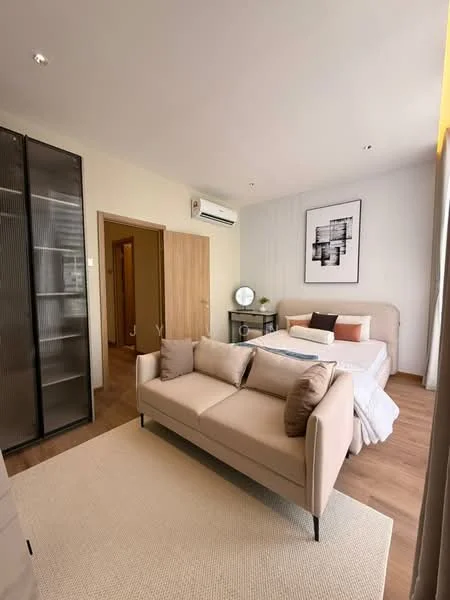 Living features: beige fabric sofa with cushions, area rug, wooden flooring, wall-mounted split AC, framed artwork on wall, large window with sheer curtains, light-colored walls, built-in wardrobe with glass doors; style: modern. Bedroom features: queen-size bed with upholstered headboard, white bedding, decorative pillows, nightstand with lamp, wooden flooring, light-colored walls, large window with sheer curtains; style: modern. Room features: wooden door leading to another room.