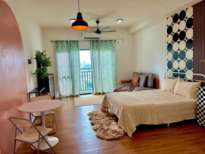 Bedroom features: king-size bed with beige bedding, upholstered headboard, 2-seater grey fabric sofa, round dining table with 2 folding chairs, wooden flooring, green sheer curtains, floor-to-ceiling windows, ceiling fan with light, wall-mounted air conditioning unit, decorative wall with circular patterns, area rug with fluffy texture, green potted plant, balcony access with city view; style: modern; view: city.