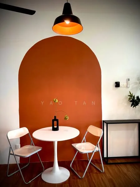 Dining features: round white dining table, two white folding chairs, orange accent wall, wooden flooring, black metal side table, single pendant light, decorative vase, flower in vase; style: modern.