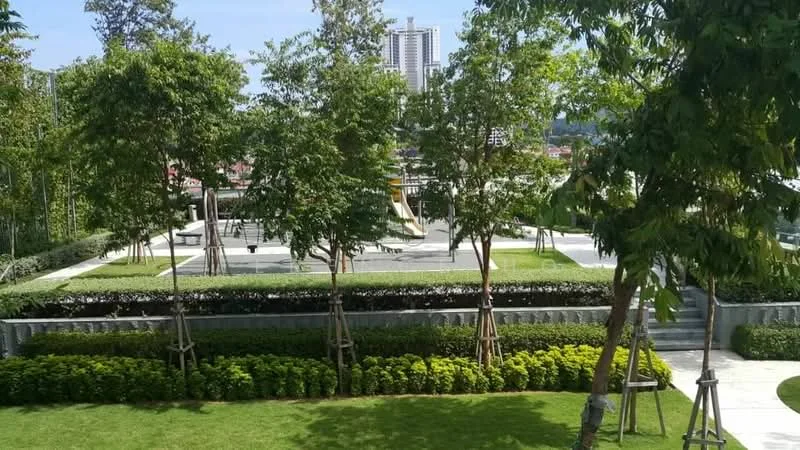 Exterior type: landscape garden; features: manicured lawn, mature trees, children's playground, paved walkway, landscaped garden beds, play equipment, surrounding greenery, city skyline in background; style: modern.