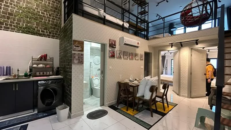 Living features: open-plan layout, grey cabinetry, white walls with decorative accents, black and white tiled backsplash, stainless-steel washing machine, dining table with upholstered chairs, area rug with geometric pattern, pendant light fixture, wall-mounted air conditioning unit, decorative wall art, floor-to-ceiling windows, wooden staircase; style: modern. Kitchen features: grey cabinetry, black countertop, stainless-steel sink, built-in oven, 4-burner gas hob, microwave, open shelving, kitchen utensils visible; style: modern. Bathroom features: white tiled walls, ceramic tile flooring, single-sink vanity, framed mirror, toilet, shower area, glass shower enclosure; style: modern. Room features: wooden flooring, decorative wall accents, open loft space above.