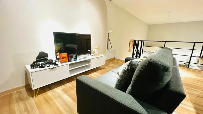 Living features: grey fabric sofa, white TV console, wall-mounted TV, wooden flooring, decorative items on console, black railing, recessed lighting, neutral wall color; style: modern.