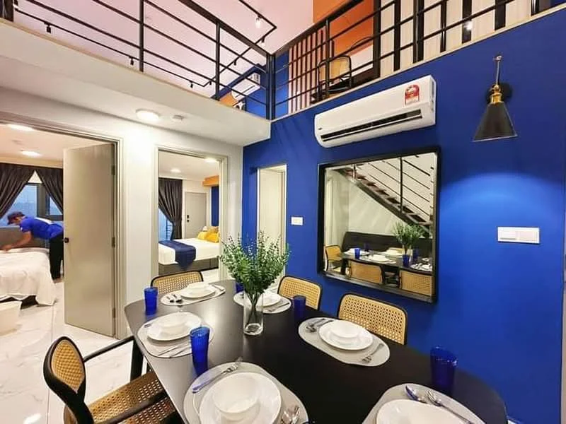 Dining features: round dining table, 8 dining plates, blue drinking glasses, wooden dining chairs with cane backing, pendant light, mirror on wall, air conditioning unit, white painted walls, grey flooring, staircase in background, dark blue accent wall; style: modern. Living features: sofa, coffee table, TV console, floor-to-ceiling windows, curtains, decorative plants; style: modern.