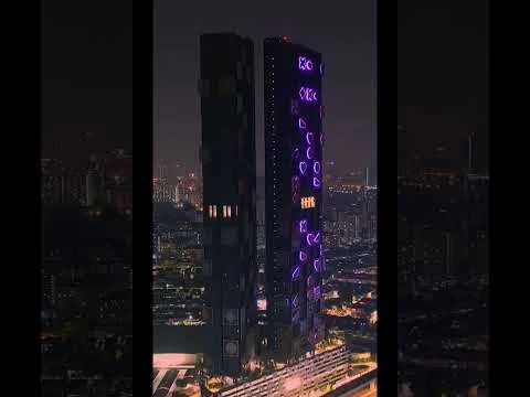 Exterior type: high-rise condominium; features: glass curtain wall, illuminated facade with purple lighting, recessed balconies, multiple storeys, surrounded by urban landscape, night view, modern architectural design; style: modern.