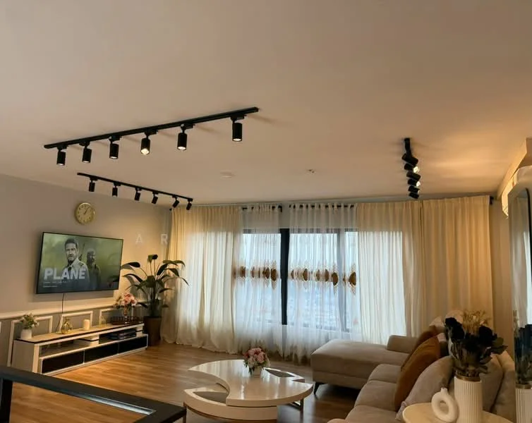 Living features: light wood flooring, recessed LED downlights, track lighting, floor-to-ceiling windows, sheer curtains, wall-mounted TV, TV console, 3-seater fabric sofa in beige, coffee table, decorative plants, wall clock, decorative vase with flowers; style: modern; view: city.