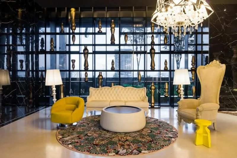Living features: black marble accent wall, large glass windows, chandelier with multiple bulbs, white tufted sofa, yellow accent chair, round coffee table, decorative area rug with floral pattern, green accent chair, two floor lamps, golden decorative objects on wall; style: modern; view: city.