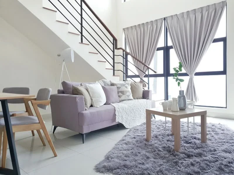 Living features: 3-seater fabric sofa in lavender, decorative throw pillows, white knitted throw blanket, wooden coffee table, area rug with fluffy texture, floor-to-ceiling windows, sheer curtains, wooden dining table with 4 chairs, modern floor lamp, staircase with metal railing, light-colored tiled flooring; style: modern.