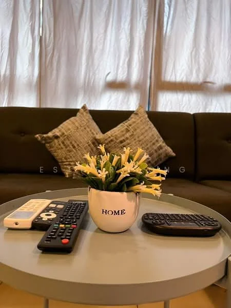 Living features: 3-seater fabric sofa in dark green, decorative throw pillows in grey, round coffee table, decorative plant in pot with 'HOME' text, remote controls on the table, curtains in light fabric, wooden flooring, soft lighting; style: modern.