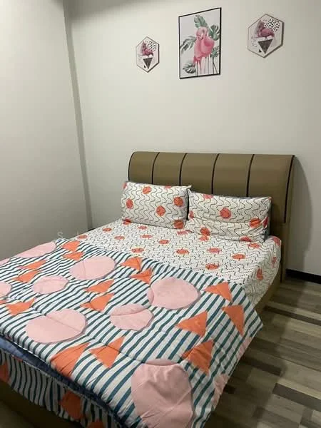 Bedroom features: king-size bed, upholstered headboard, decorative bedding with geometric patterns, two patterned pillows, wooden flooring, wall-mounted artwork with floral and flamingo design, neutral painted walls, nightstand with lamp (not visible), window (not visible); style: modern.