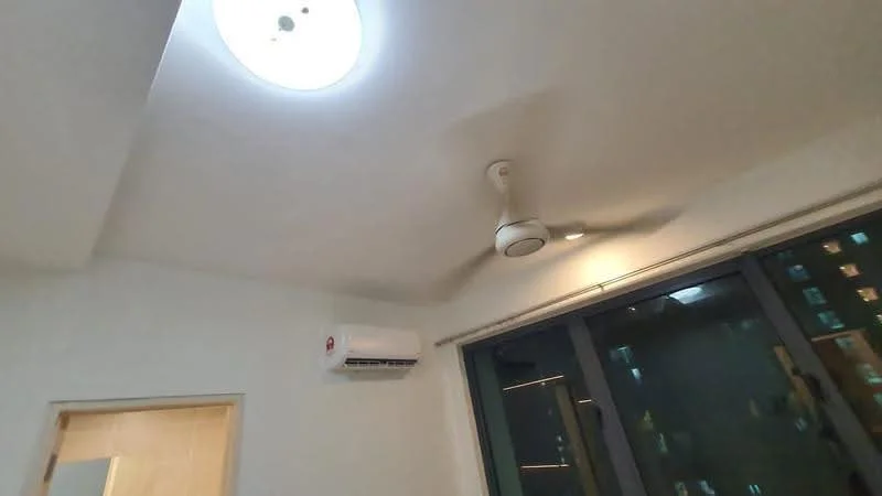Room features: ceiling light fixture, ceiling fan, wall-mounted split AC, large glass windows, white painted walls.