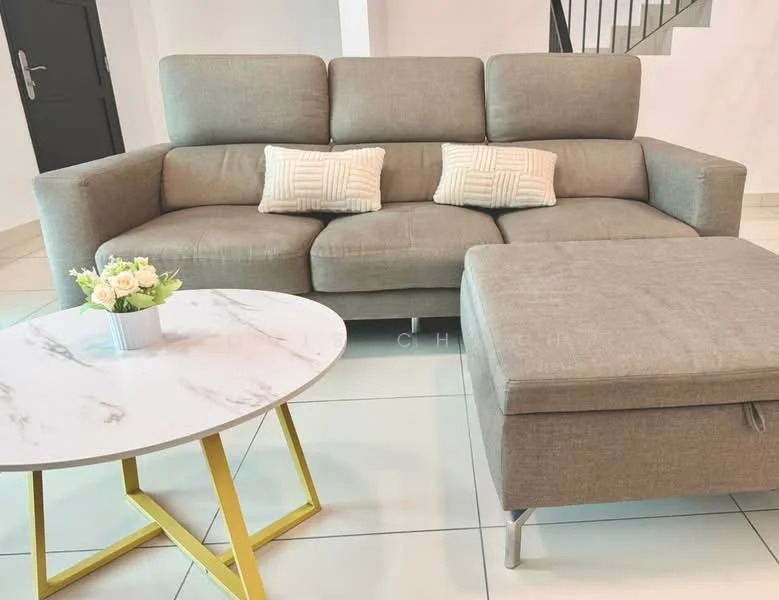 Living features: 3-seater fabric sofa in light grey, 2 decorative cushions with geometric pattern, round coffee table with marble top, yellow metal legs on coffee table, ottoman in matching fabric, white tiled flooring, neutral painted walls, staircase in background; style: modern.