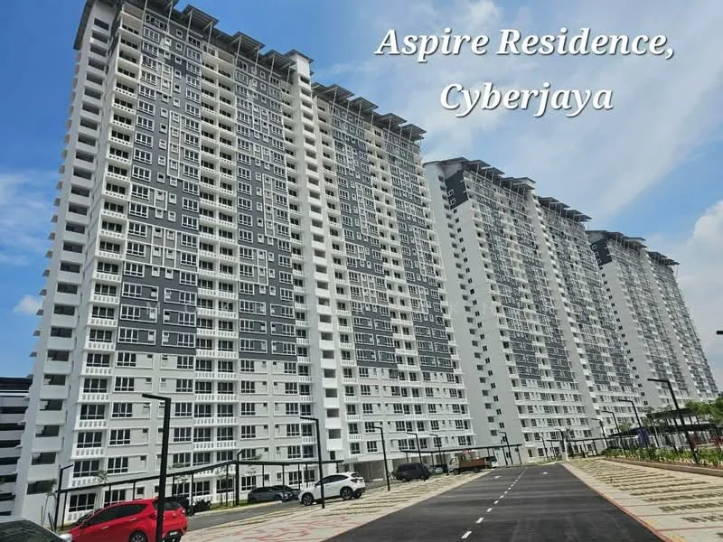 Exterior type: high-rise condominium; features: grey and white painted facade, multiple storeys, balconies on each unit, large windows, landscaped entrance, paved driveway, parking spaces visible, surrounded by greenery; style: modern.