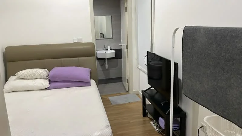Bedroom features: queen-size bed with upholstered headboard, two purple pillows, wooden flooring, wall-mounted TV, black TV console, small white wastebasket, door leading to bathroom, light-colored walls, window with natural light; style: modern. Bathroom features: wall-mounted sink, mirror above sink, grey tiled walls, grey tiled flooring, toilet, light fixture.