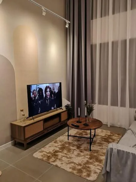 Living features: light grey fabric sofa, wooden coffee table, TV console with storage, wall-mounted TV, area rug with geometric pattern, floor-to-ceiling windows, sheer curtains, accent wall with beige and cream shapes, recessed lighting, decorative candles, small potted plants; style: modern.