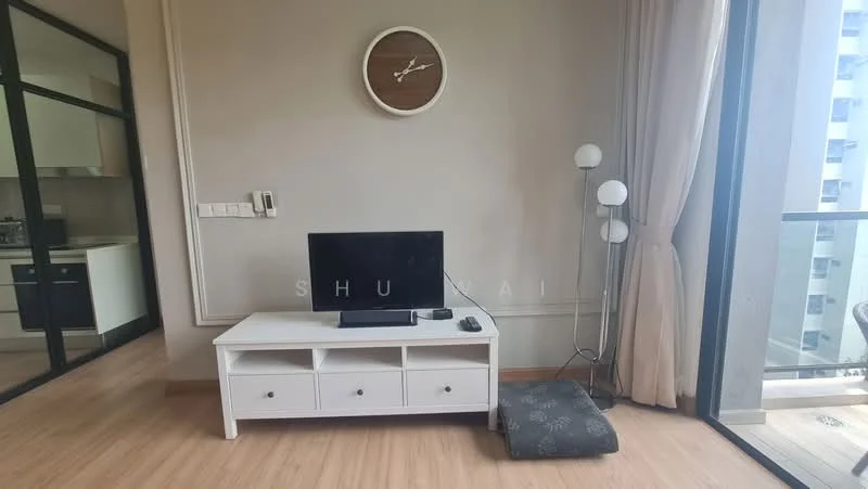 Living features: wooden flooring, light grey painted walls, wall clock, white TV console with drawers, flat-screen TV, floor lamp, large glass sliding door, curtains, decorative cushion on the floor; style: modern. Kitchen features: open layout, visible kitchen area, white cabinetry, stainless-steel appliances; style: modern.