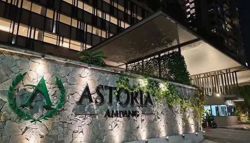 Exterior type: high-rise condominium; features: stone cladding facade, illuminated signage, landscaped entrance with greenery, covered entrance area, modern architectural design, multiple storeys visible, night lighting, glass curtain wall, manicured landscaping; style: modern.