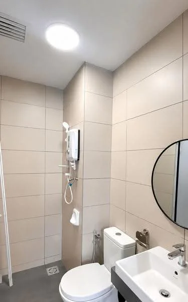 Bathroom features: light grey tile flooring, beige tiled walls, round mirror, single-sink vanity with white cabinet, chrome basin mixer faucet, one-piece toilet, shower with handheld showerhead, wall-mounted shower unit, towel rack, toilet paper holder, recessed ceiling light; style: modern.