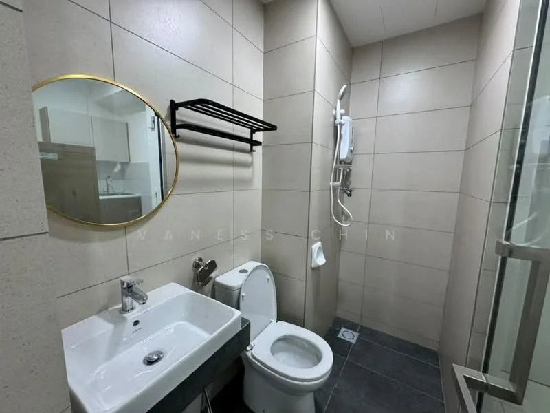 Bathroom features: grey tiled walls, white ceramic sink, chrome faucet, round mirror with gold frame, white toilet, shower with glass enclosure, wall-mounted showerhead, towel rack, dark grey floor tiles; style: modern.