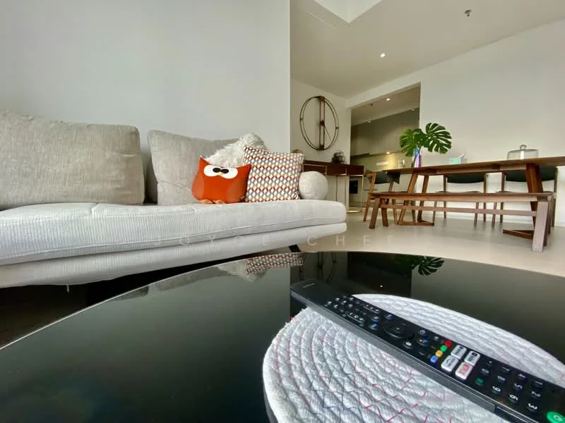 Living features: 3-seater fabric sofa in light grey, decorative orange and white pillow, round coffee table with black surface, remote control on coffee table, dining table with wooden legs, 4 dining chairs, green plant in corner, wall-mounted artwork or mirror, recessed downlights, open kitchen area visible in background; style: modern.