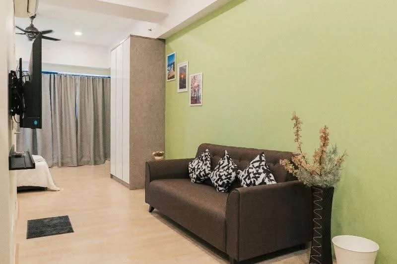 Living features: green painted walls, laminate flooring, 3-seater fabric sofa in brown, decorative cushions with geometric pattern, wall-mounted TV, ceiling fan, curtains in grey, framed artwork on walls, decorative vase with plants, area rug in black, built-in wardrobe, light fixtures; style: modern.