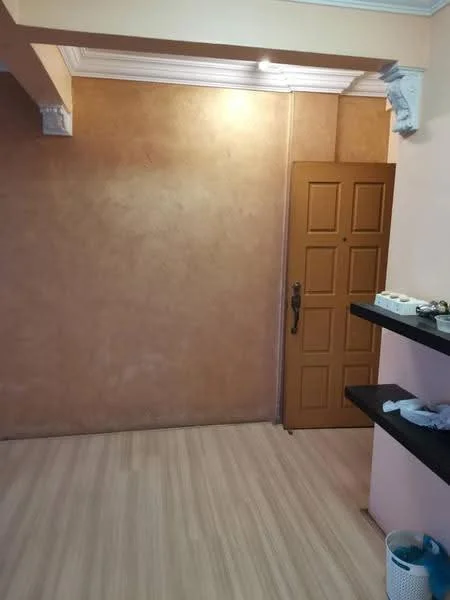 Room features: orange textured wall, wooden door with multiple panels, light-colored laminate flooring, white ceiling with crown moulding, shelf with items, basket, wall-mounted light fixture.