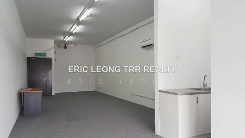 Room features: grey carpet flooring, white painted walls, exposed ceiling with fluorescent lighting, wall-mounted split AC, kitchenette with countertop, stainless-steel sink, single-bowl stainless-steel sink, cabinetry under countertop, door leading to hallway; style: minimalist.