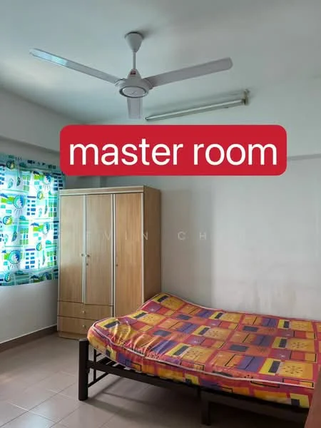 Bedroom features: single bed with colorful bedding, wooden bed frame, wooden wardrobe with two doors, 5-blade ceiling fan, window with colorful patterned curtains, cream painted walls, tile flooring, fluorescent ceiling light.