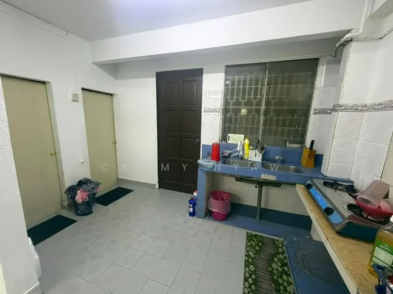 Kitchen features: grey tiled flooring, white painted walls, single-bowl stainless-steel sink, chrome pull-down faucet, wooden countertop, built-in gas stove, window with grid pattern, two closed doors, pink waste bin, cleaning supplies on countertop, area rug with green pattern.
