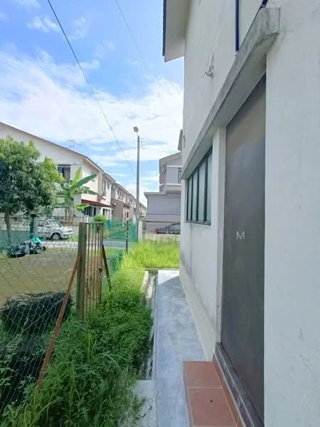 Exterior features: concrete wall, single door, window with green frame, pathway with concrete surface, overgrown grass, fence, surrounding residential buildings, clear blue sky.