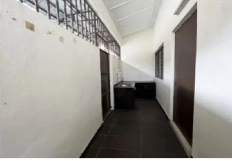 Room features: white painted walls, black tiled flooring, sliding wooden door, window with metal grille, high ceiling, utility sink, countertop, storage cabinet.