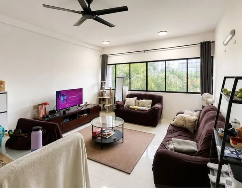 Living features: 3-seater fabric sofa in dark brown, 2-seater fabric sofa in dark brown, coffee table with glass top, TV console, wall-mounted TV, area rug with circular pattern, ceiling fan with 5 blades, large windows with sheer curtains, white painted walls, tile flooring, decorative plants, shelves with decorative items; style: modern; view: garden.