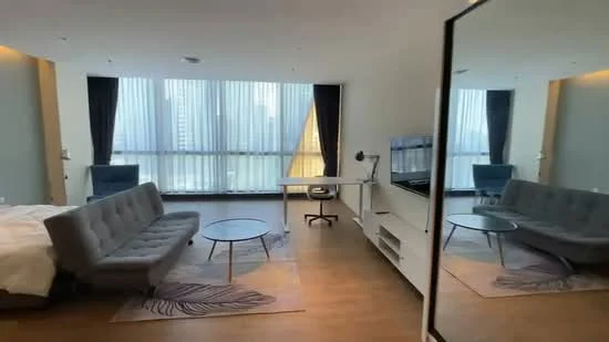 Living features: grey fabric sofa, round coffee table, area rug with leaf pattern, floor-to-ceiling windows, sheer curtains, blackout curtains, TV mounted on wall, white media console, desk with lamp, blue accent chair, wooden flooring, decorative mirror; style: modern; view: city.