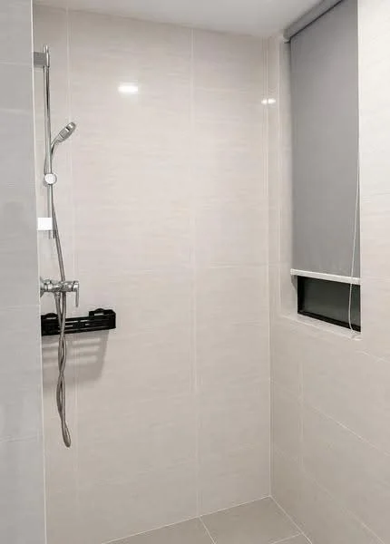 Bathroom features: light grey tile cladding on walls, light grey tile flooring, walk-in shower with glass enclosure, rain shower head, handheld shower, chrome shower faucet, built-in shower shelf, window with roller blind; style: modern.