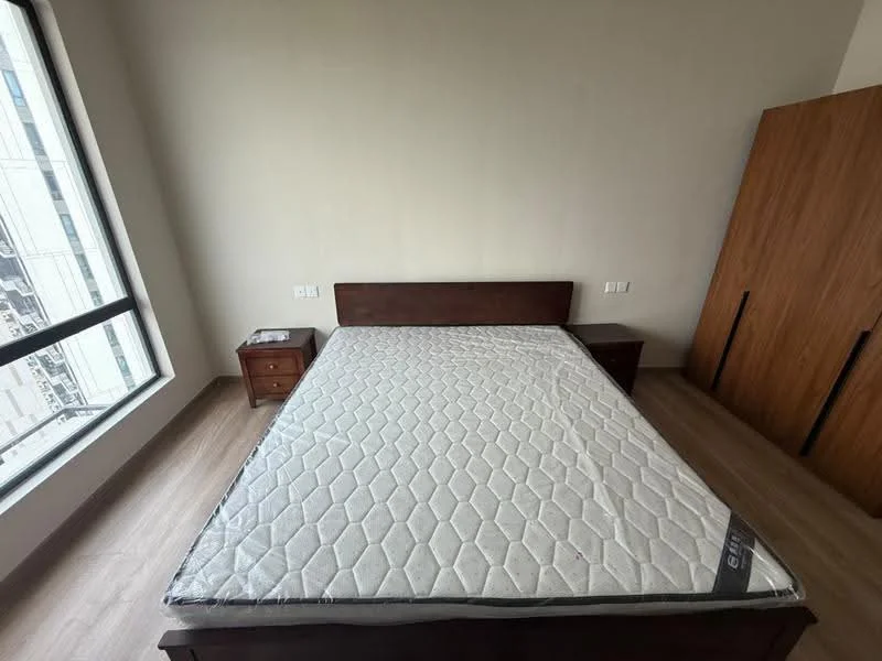 Bedroom features: queen-size bed, wooden bed frame, two bedside tables, laminate flooring, large window with city view, built-in wardrobe with wooden doors, neutral painted walls, no visible decor; style: modern; view: city.