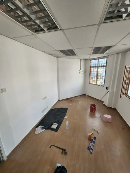 Room features: white painted walls, wooden flooring, ceiling tiles with grid pattern, window with grid design, unfinished space with construction materials, bucket, tools on the floor, water bottle.